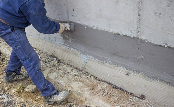 Construction worker with brush applied hydro insulation on wall
